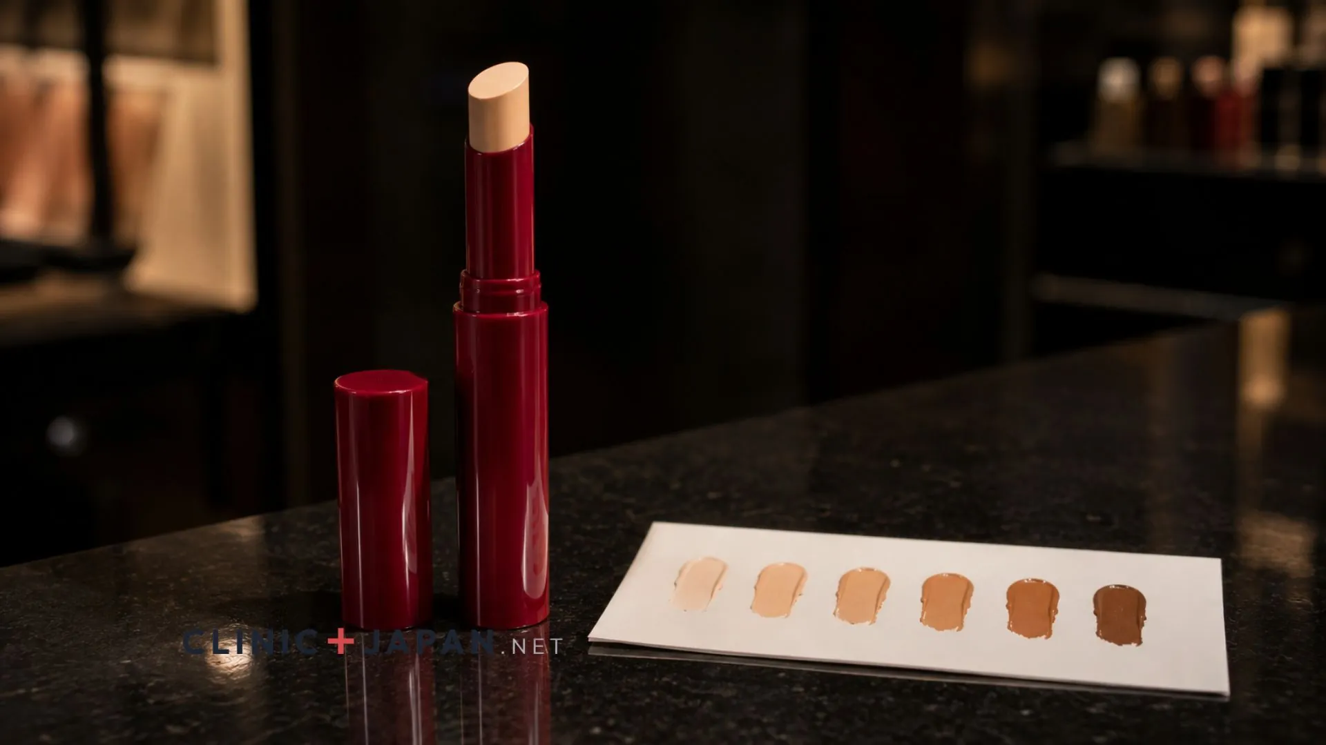 Cle de Peau Beaute concealer stick in its red case on a department store counter beside shade swatches on a testing card