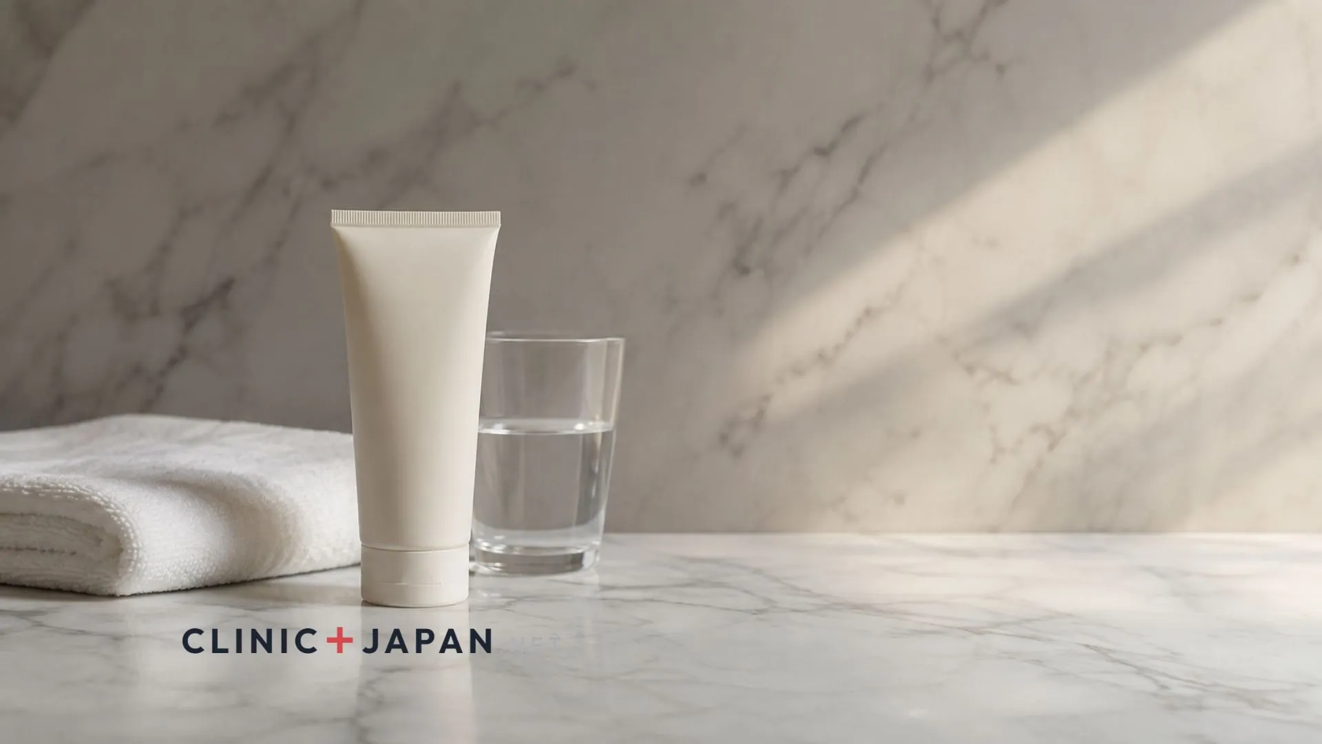 Tatcha Rice Wash tube on a pale marble bathroom surface next to a folded towel and a glass of water